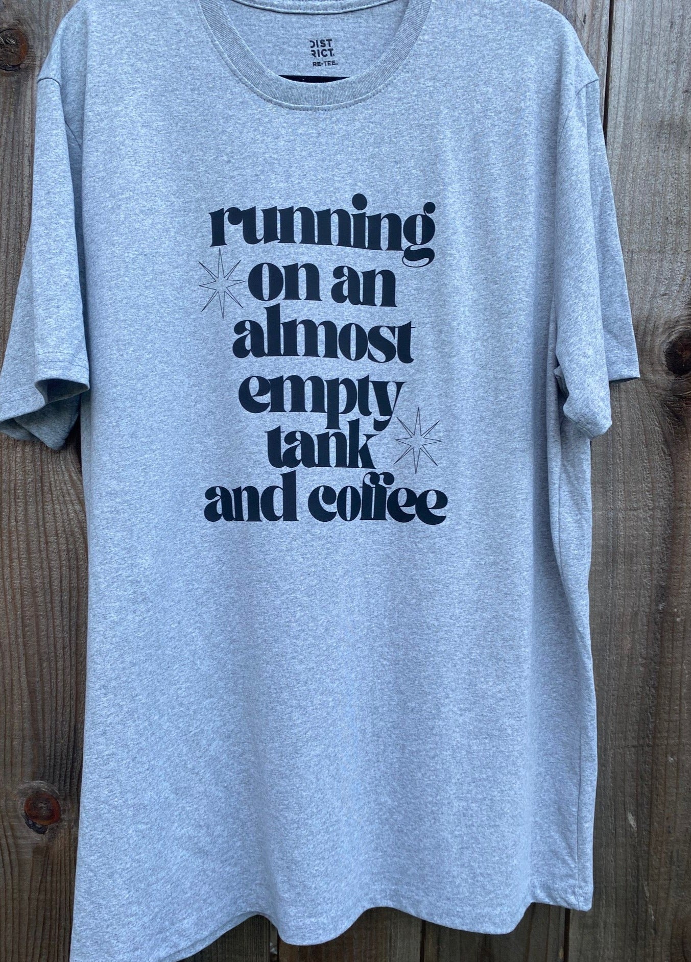 Gray t-shirt with "running on an almost empty tank and coffee" printed in black on the front with 2 black outlined star bursts