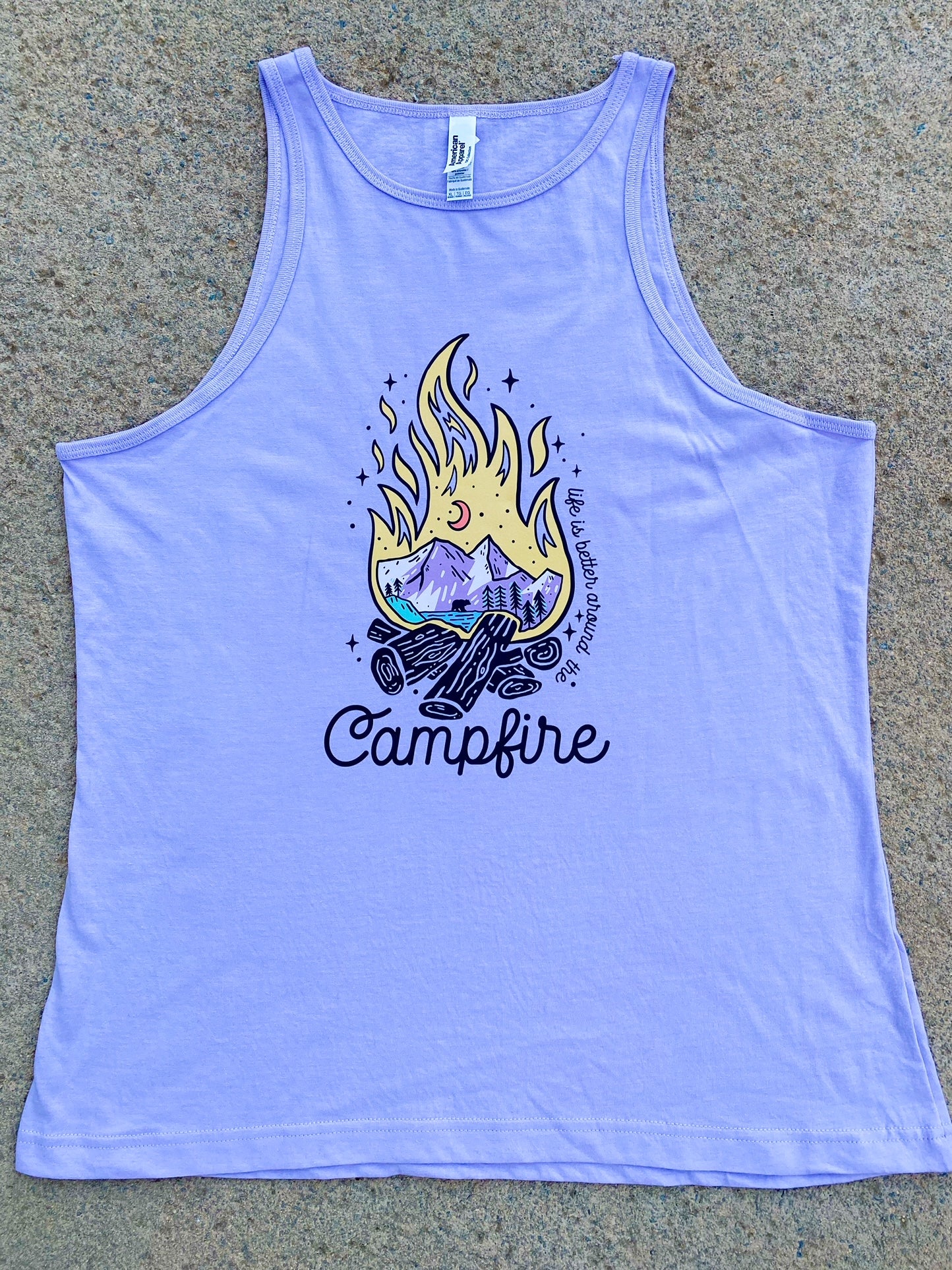 Lilac Tank Top with a campfire in the middle. The flame shows an outdoor scene of the mountains and moon. Along the right side of the flame it says "life is better around the" and then at the bottom of the flame it says "campfire"