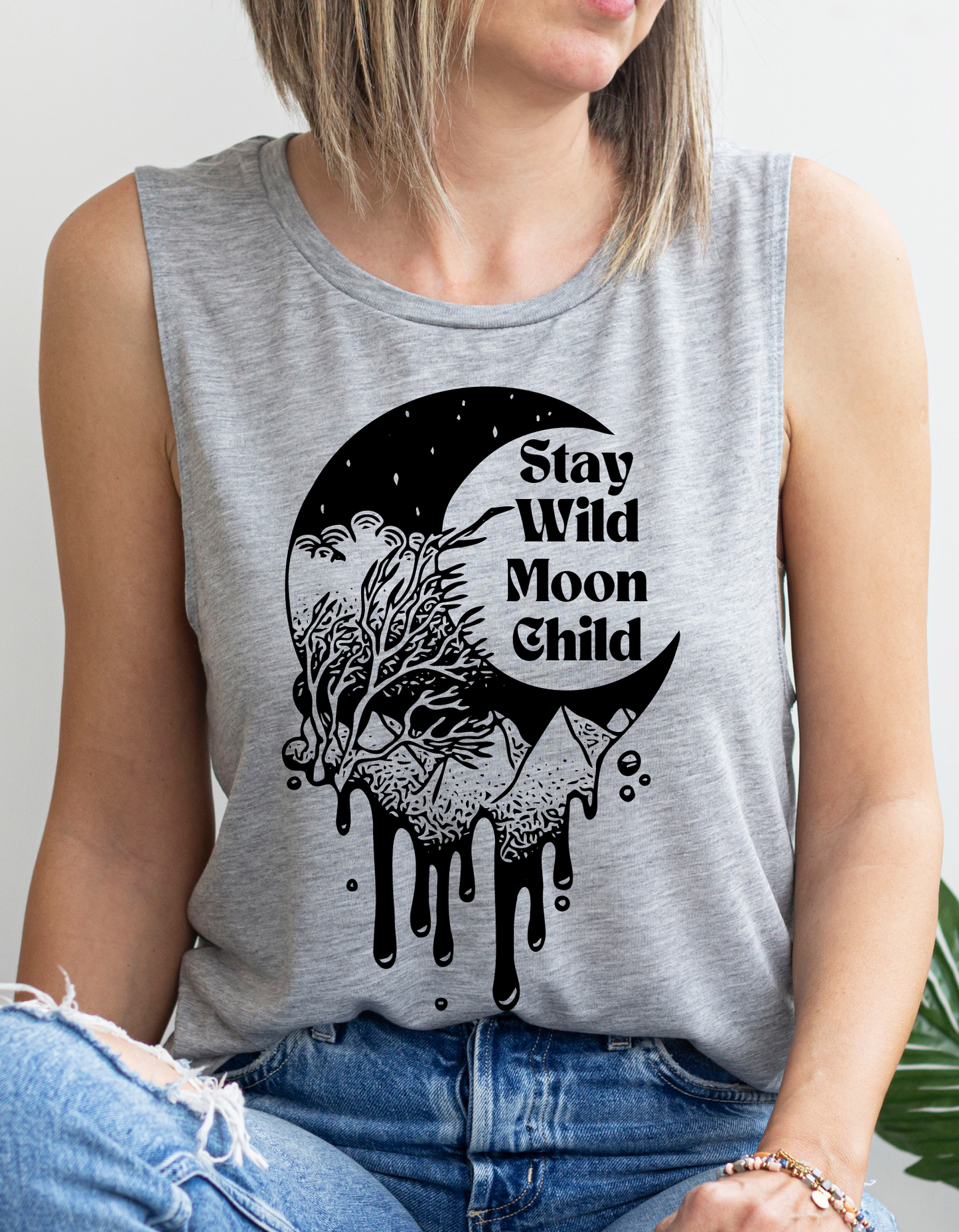 Black crescent moon with trees and mountains dripping. In the middle of the crescent are the words "stay wild moon child". All black graphic on a grey tank top.