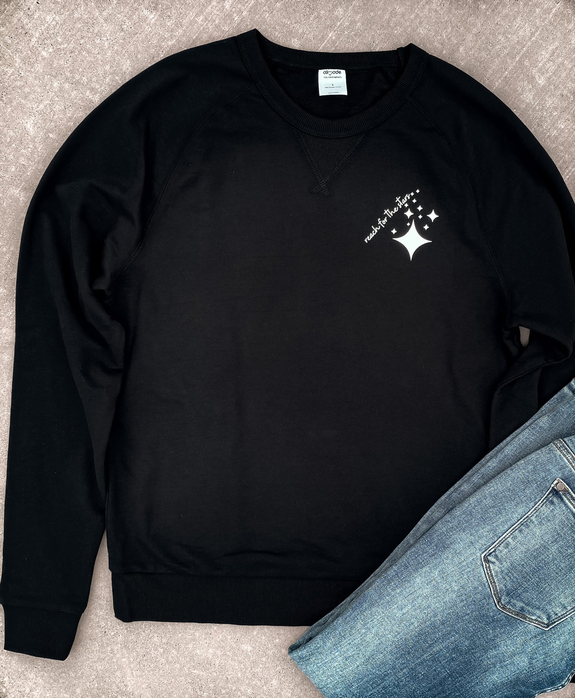 Black Organic French Terry Sweatshirt with Reach for the Stars screen printed on the upper left hand side of the sweatshirt surrounded by white mid-century stars